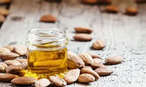 Un frasco de aceite de almendras para la cara rodeado de almendras enteras sobre una superficie de madera rústica.