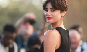 Mujer con un moderno corte bixie, labios rojos y mirada intensa, rodeada de fotógrafos.