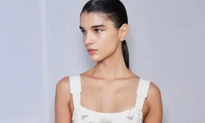Mujer con coleta alta lisa, maquillaje sutil y vestido blanco bordado.