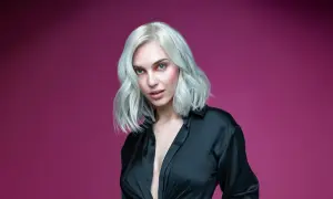 Mujer con cabello rubio platino y ojos azules, vestida con una camisa negra. Aprende como matizar el pelo en casa para lograr este look.
