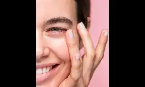 Una mujer sonríe mientras se aplica suavemente un producto en el contorno de ojos. Las opiniones sobre contorno ojos freshly son muy positivas.