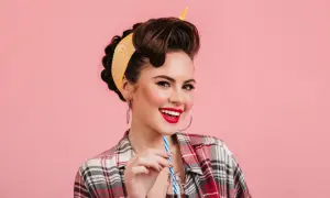 Mujer sonriente con peinados vintage y pañuelo amarillo, bebiendo de una botella.