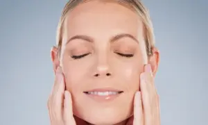 Mujer con ojos cerrados y una sonrisa suave, acariciando su rostro para realzar su óvalo facial.