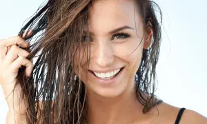 Mujer sonríe con pelo efecto mojado, luciendo su cabello castaño oscuro y húmedo.