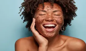 Mujer sonríe con la cara cubierta de un exfoliante, mostrando lo que es exfoliar la piel para una tez radiante.