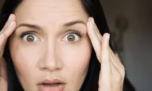 Mujer con ojos muy abiertos y arrugas en la frente, tocándose las sienes con las manos.