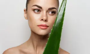 Mujer con piel radiante sostiene una hoja de aloe vera, demostrando que se puede usar aloe vera directamente de la planta para un cuidado natural.