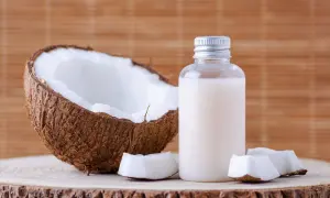 Aceite de coco en botella junto a coco partido. Considera las contraindicaciones del aceite de coco antes de usarlo.