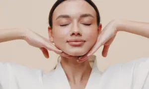 Mujer con ojos cerrados, disfrutando de un masaje facial. Sus manos sostienen suavemente su rostro, practicando yoga facial para una piel radiante.