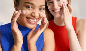 Dos mujeres sonríen mientras se aplican crema en el rostro. Ambas tienen piel normal y lucen radiantes.