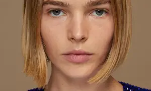 Primer plano de una mujer con un elegante bob peinado, ojos penetrantes y un vestido azul brillante.