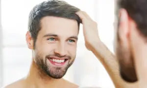 Hombre sonriente se toca el cabello, reflejando su confianza en sus tratamientos de belleza para hombres.