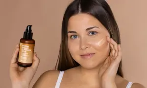 Mujer aplica bronceador freshly en su mejilla. Sostiene un frasco de crema autobronceadora.
