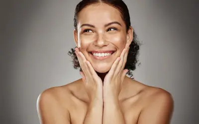 Mujer sonríe con las manos en las mejillas, disfrutando de los efectos de la radiofrecuencia facial para una piel radiante y rejuvenecida.