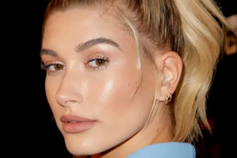 Primer plano de una mujer con piel de cristal, ojos marrones y cabello rubio recogido.