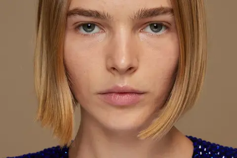 Primer plano de una mujer con un elegante bob peinado, ojos penetrantes y un vestido azul brillante.