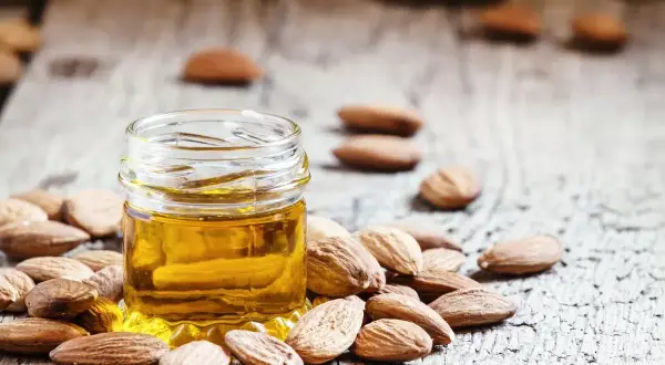 Un frasco de aceite de almendras para la cara rodeado de almendras enteras sobre una superficie de madera rústica.