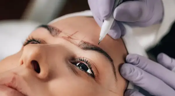 Manos enguantadas dibujan el contorno de las cejas para un procedimiento de powder brows.