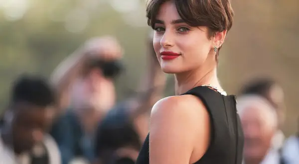 Mujer con un moderno corte bixie, labios rojos y mirada intensa, rodeada de fotógrafos.