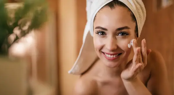 Mujer sonriente se aplica crema en el rostro. Descubre para qué sirve el retinol para una piel radiante.