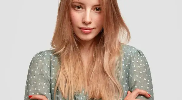 Mujer joven con peinados pelo liso, rubio y degradado, con un vestido verde de flores blancas.