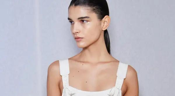 Mujer con coleta alta lisa, maquillaje sutil y vestido blanco bordado.