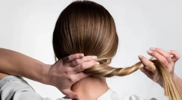 Manos trenzando el cabello para crear peinados para dormir que protejan el pelo.