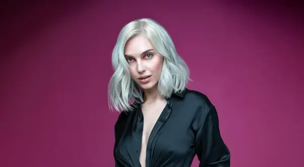 Mujer con cabello rubio platino y ojos azules, vestida con una camisa negra. Aprende como matizar el pelo en casa para lograr este look.
