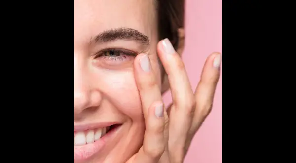 Una mujer sonríe mientras se aplica suavemente un producto en el contorno de ojos. Las opiniones sobre contorno ojos freshly son muy positivas.