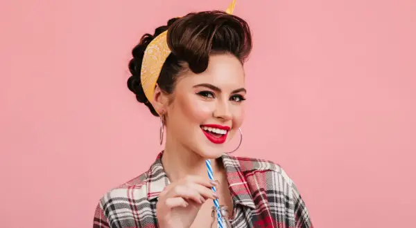 Mujer sonriente con peinados vintage y pañuelo amarillo, bebiendo de una botella.