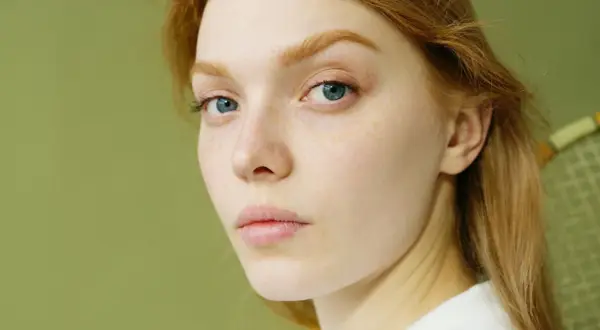 Primer plano de una joven pelirroja con pecas y ojos azules. Su piel parece saludable, sin signos de glicación.