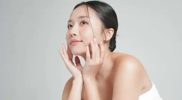 Mujer asiática con piel radiante, acariciando su rostro. Su secreto: agua de arroz para la cara.