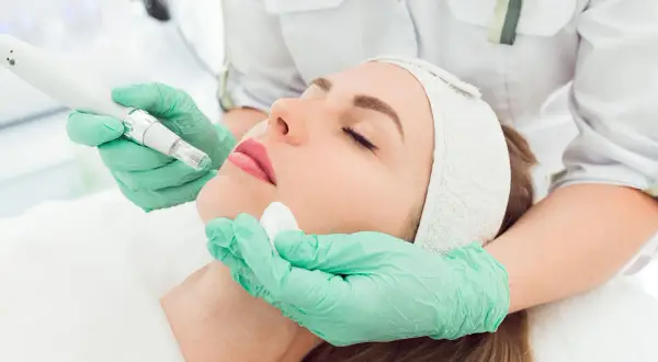 Una esteticista aplica un tratamiento facial con un dispositivo de microagujas, mostrando los beneficios de la mesoterapia para una piel radiante.