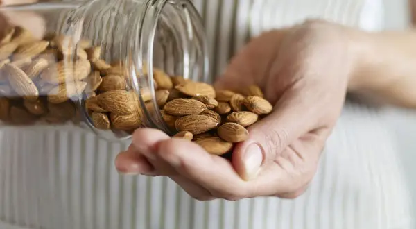 Manos sostienen almendras cayendo de un frasco. Considera las desventajas del aceite de almendras antes de usarlo.