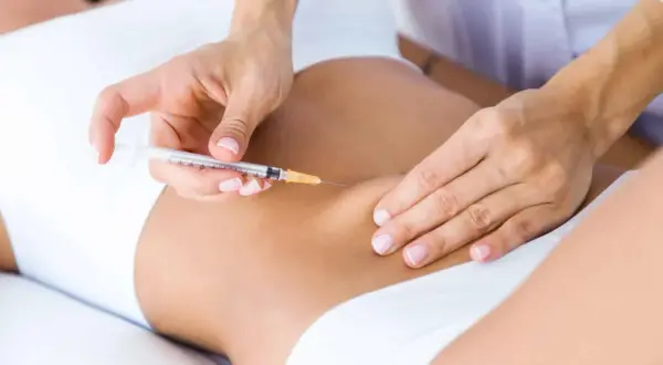 Manos expertas aplican carboxiterapia corporal con jeringa en la zona abdominal para mejorar la piel.