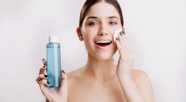 Mujer sonriente se aplica agua micelar Deliplus con un algodón. Piel radiante y fresca.