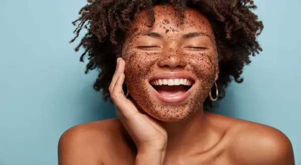 Mujer sonríe con la cara cubierta de un exfoliante, mostrando lo que es exfoliar la piel para una tez radiante.