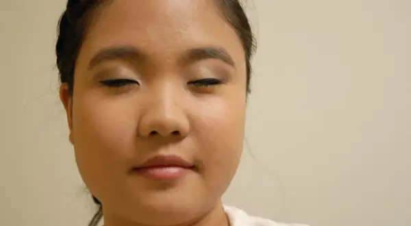 Primer plano de una mujer con los ojos cerrados y maquillaje en los párpados y delineador.