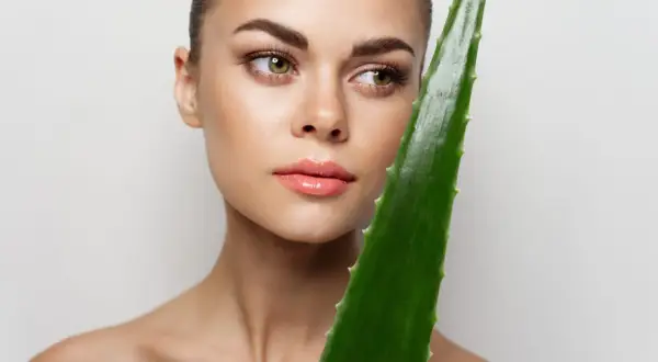 Mujer con piel radiante sostiene una hoja de aloe vera, demostrando que se puede usar aloe vera directamente de la planta para un cuidado natural.