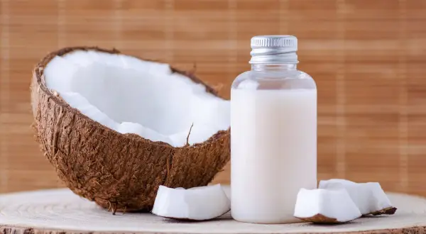 Aceite de coco en botella junto a coco partido. Considera las contraindicaciones del aceite de coco antes de usarlo.