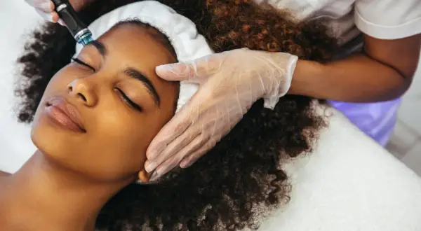Una mujer disfruta de un tratamiento Hydrafacial. Un profesional con guantes aplica el dispositivo en su rostro para una piel radiante.