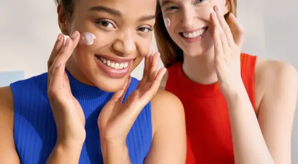 Dos mujeres sonríen mientras se aplican crema en el rostro. Ambas tienen piel normal y lucen radiantes.