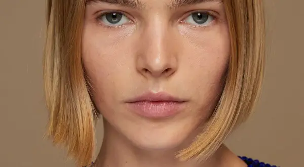 Primer plano de una mujer con un elegante bob peinado, ojos penetrantes y un vestido azul brillante.