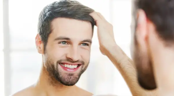 Hombre sonriente se toca el cabello, reflejando su confianza en sus tratamientos de belleza para hombres.