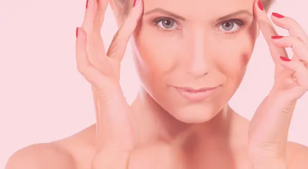 Mujer con manos en la frente, piel radiante tras carboxiterapia facial.