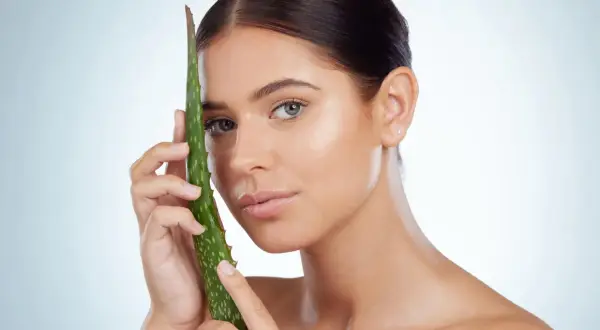 Mujer con piel radiante sosteniendo una hoja de aloe vera, ideal para el cuidado del aloe vera para la cara.