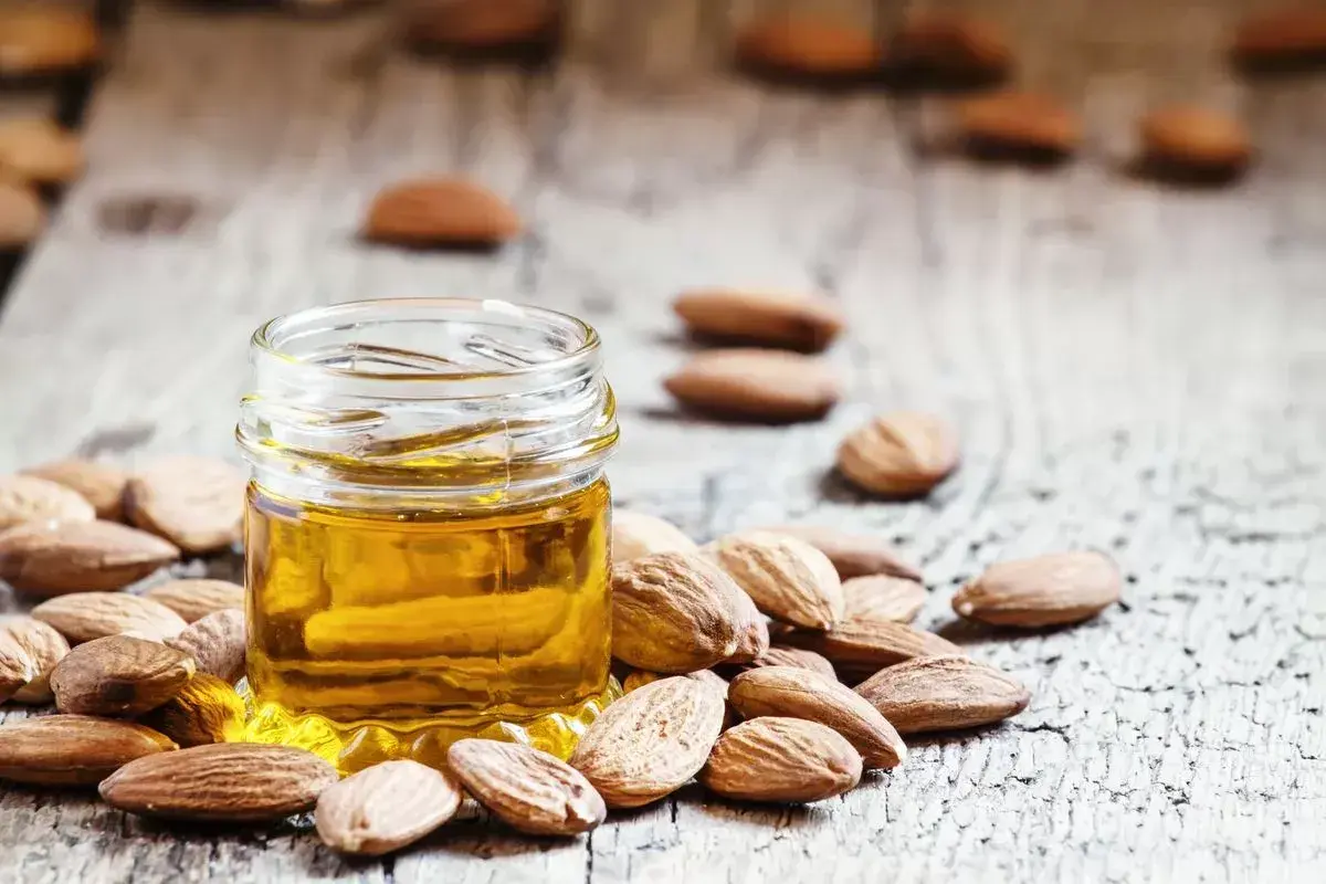 Un frasco de aceite de almendras para la cara rodeado de almendras enteras sobre una superficie de madera rústica.