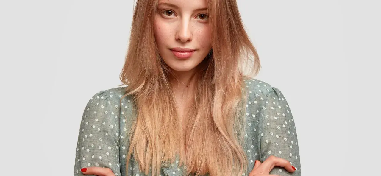 Mujer joven con peinados pelo liso, rubio y degradado, con un vestido verde de flores blancas.