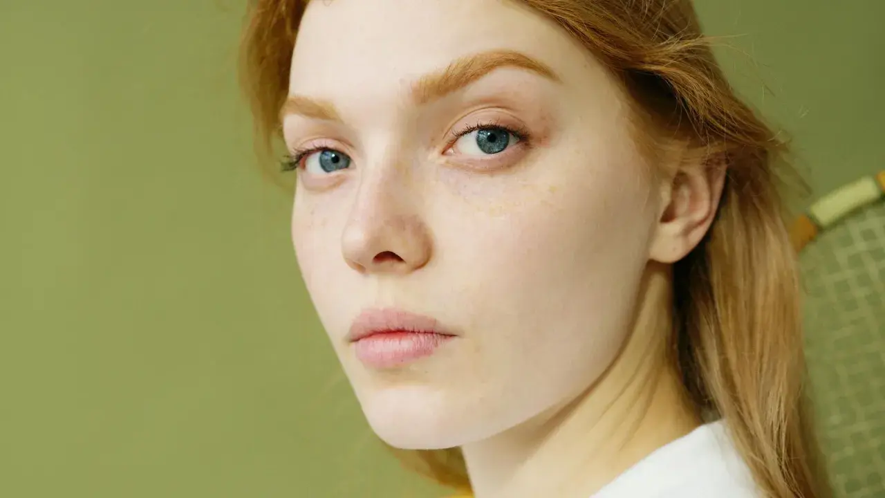 Primer plano de una joven pelirroja con pecas y ojos azules. Su piel parece saludable, sin signos de glicación.