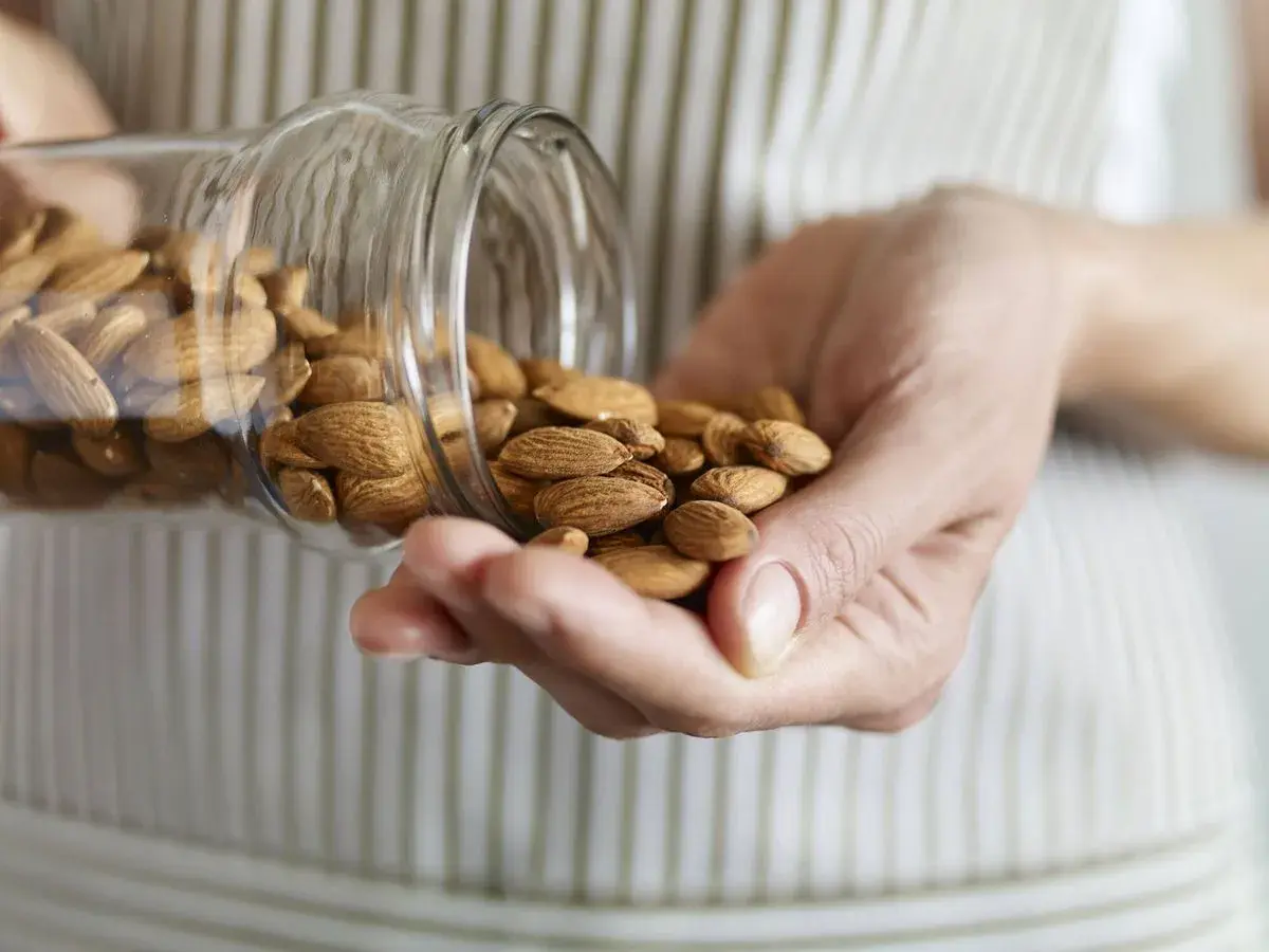 Manos sostienen almendras cayendo de un frasco. Considera las desventajas del aceite de almendras antes de usarlo.